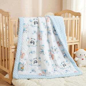 Couverture enfant matelassée à motifs de pandas bleus posée sur un lit d'enfant dans une chambre douce
