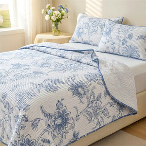 Couvre-lit matelassé à fleurs bleues et blanches posé sur un lit avec ses deux taies assorties