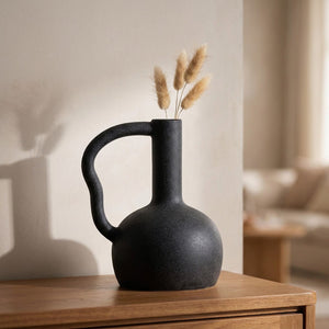 Vase en céramique noir effet grès mat avec grande anse ronde et pampa séchée posé sur une console en bois