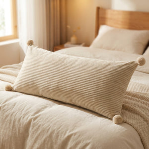 Coussin de lit long en velours côtelé beige orné de pompons posé sur un lit