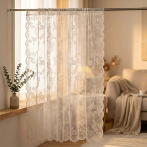 Rideau voilage en dentelle blanche à motif de roses suspendu devant une fenêtre lumineuse dans un intérieur romantique