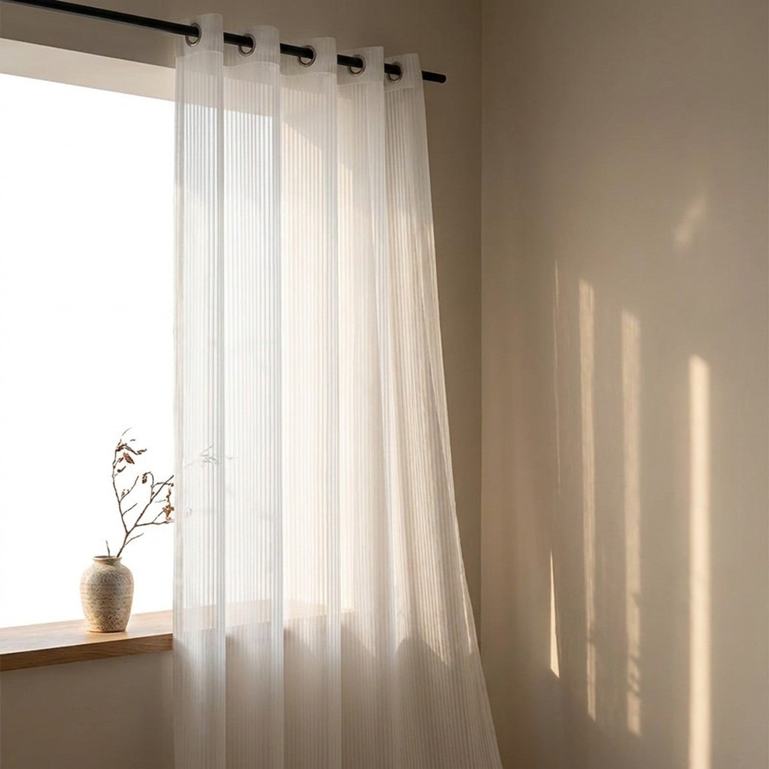 Voilage blanc à rayures suspendu par œillets métalliques devant une fenêtre ensoleillée avec un vase et une branche