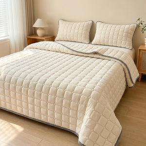 Couvre-lit matelassé en velours écru avec deux taies assorties installé sur un lit dans une chambre chaleureuse