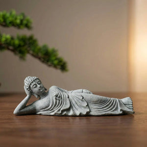 Statue de Bouddha couché en grès gris sculptée à la main posée sur une surface en bois dans une ambiance zen