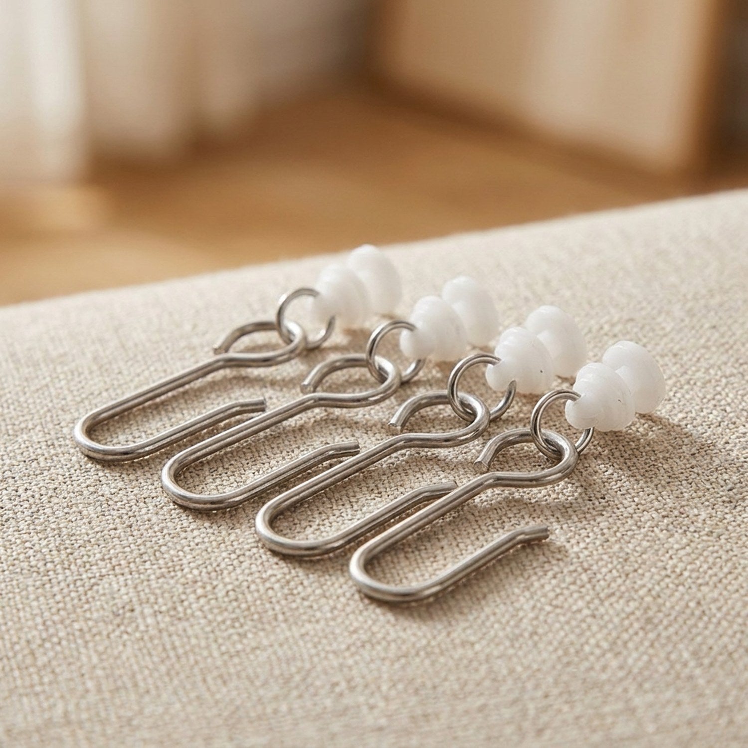 Crochets métalliques et anneaux coulissants blancs pour rail de rideau posés sur un tissu beige