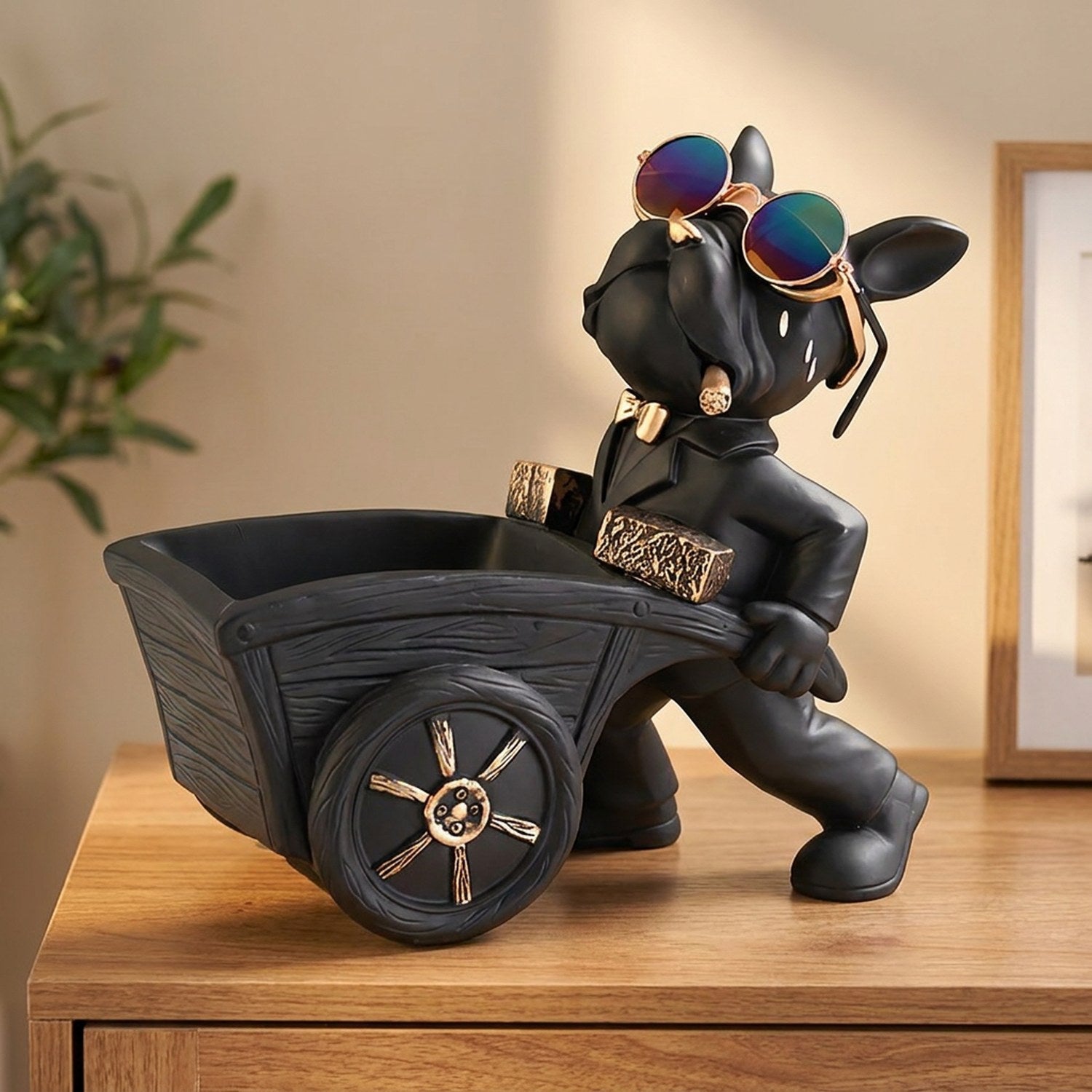 Statue de bouledogue français noir à lunettes colorées poussant une brouette vide-poche posée sur une console