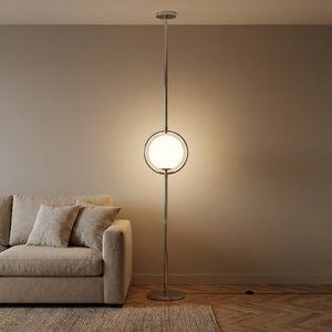 Lampadaire colonne chrome avec boule lumineuse en verre dépoli allumée dans un salon contemporain