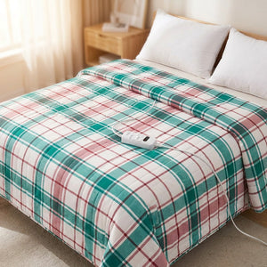 Couverture chauffante électrique au motif tartan vert et rose posée sur un lit avec sa télécommande de température