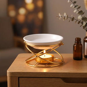 Brûleur d'huile essentielle doré en métal avec coupelle en céramique blanche et bougie allumée sur une table