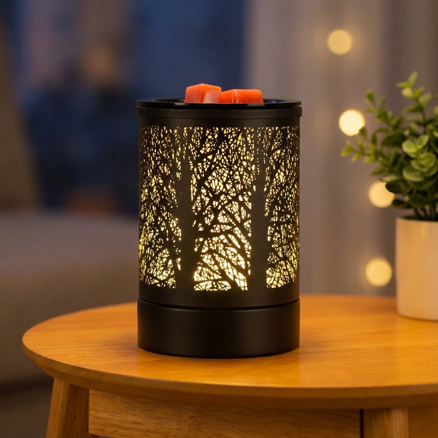 Brûle-parfum électrique noir au motif forêt avec lumière LED colorée allumée sur une table