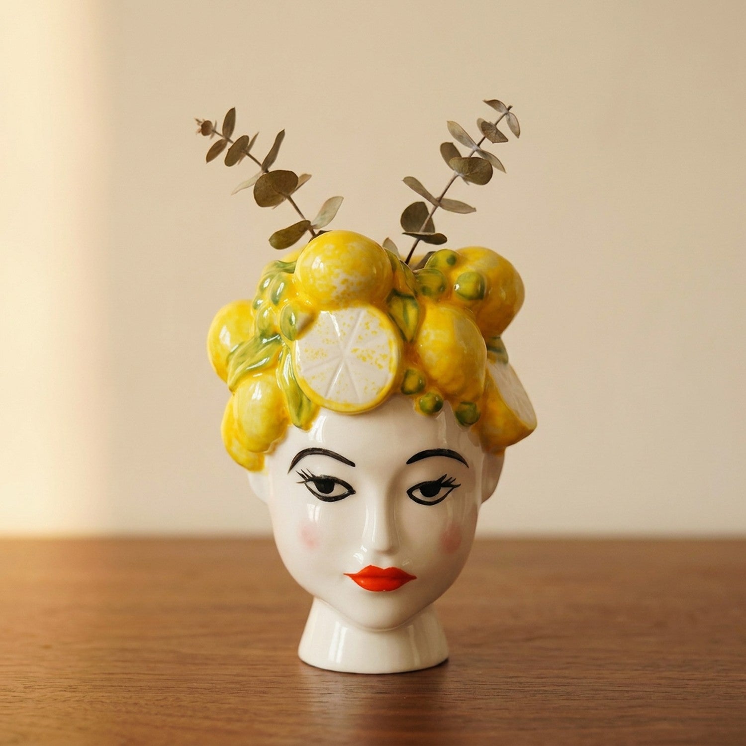 Vase en porcelaine représentant un visage de femme aux lèvres rouges couronné de citrons jaunes sur un meuble en bois
