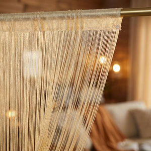 Rideau à fil scintillant suspendu à une tringle devant une porte de salon lumineuse
