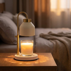 Lampe chauffe-bougie blanche au bras doré fin diffusant une lumière chaude au-dessus d'une bougie allumée