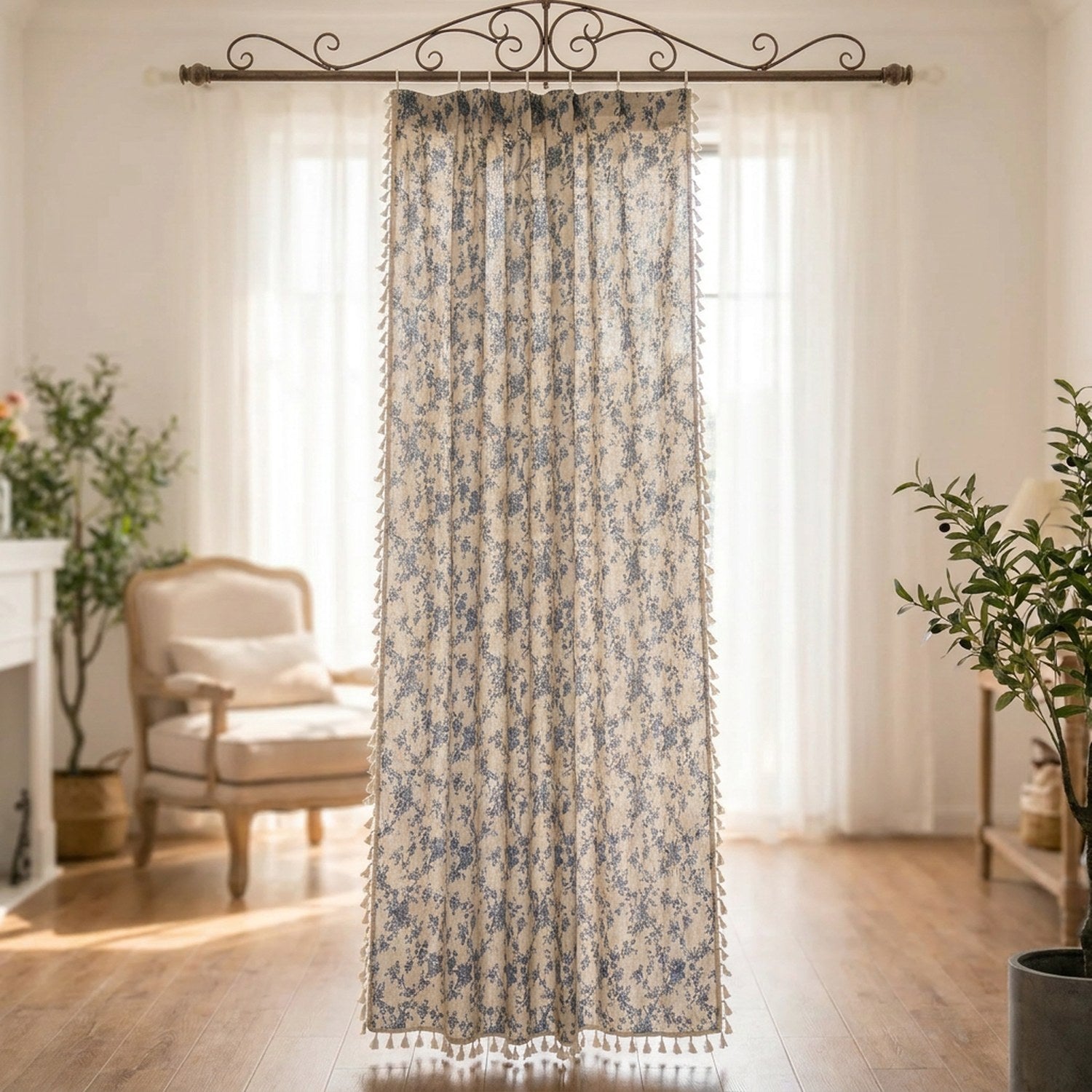 Rideau fleuri en lin et coton à motif floral bleu et bordure à pompons suspendu devant une fenêtre lumineuse