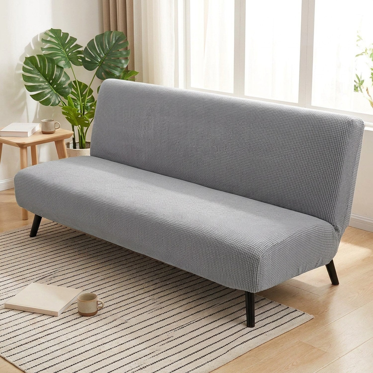 Housse de canapé lit futon grise dans un salon lumineux avec plante verte