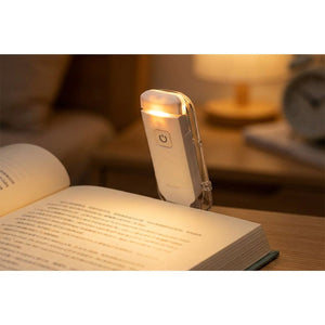 Lampe de lecture blanche à pince fixée sur un livre ouvert émettant une lumière chaude
