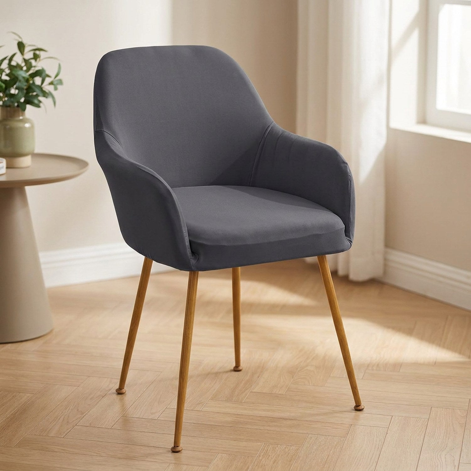 Housse de fauteuil extensible gris foncé installée sur une chaise à accoudoirs dans une salle à manger lumineuse