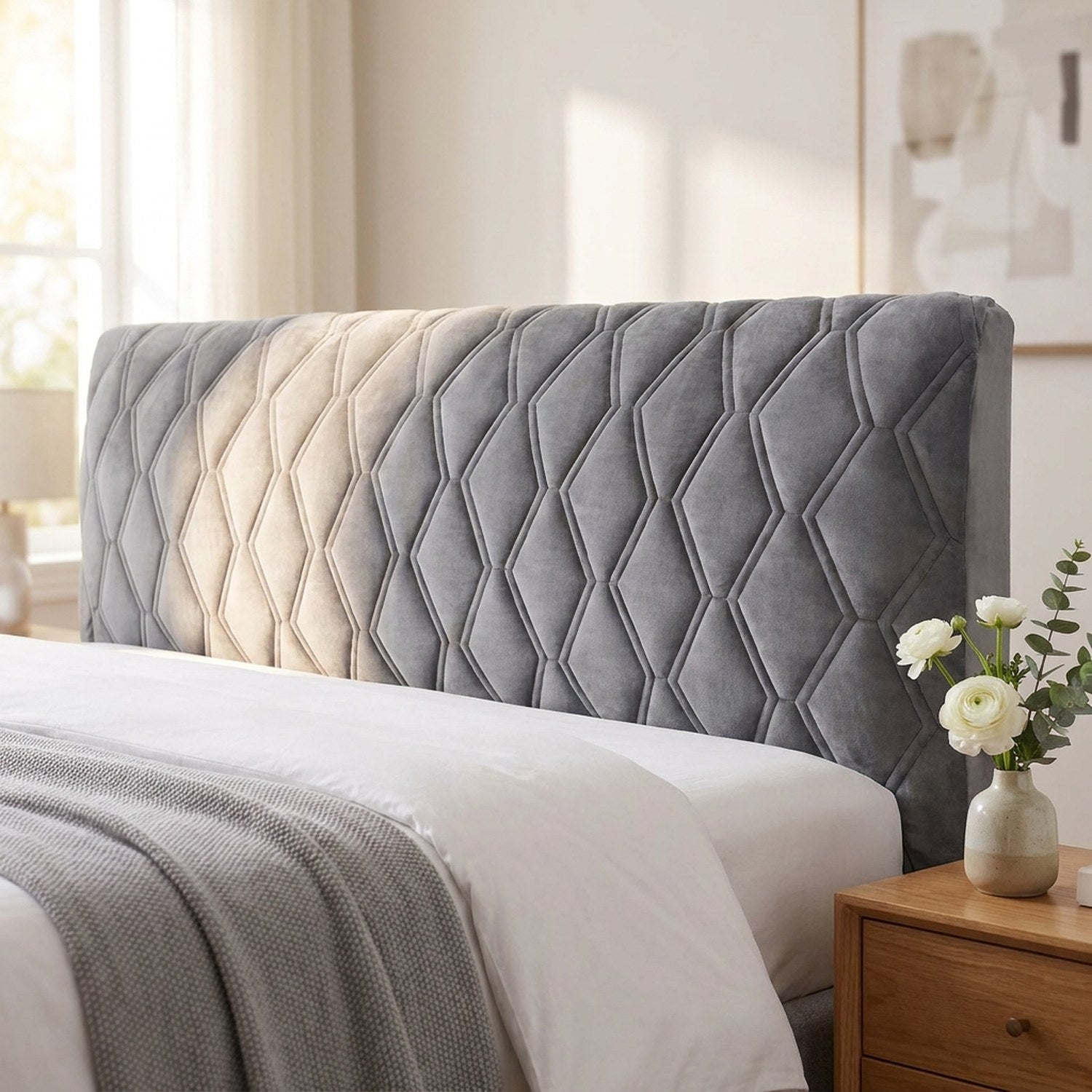 Housse de tête de lit en velours matelassé gris installée sur un lit dans une chambre lumineuse