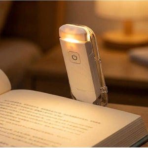 Lampe de lecture blanche à pince fixée sur un livre ouvert émettant une lumière chaude