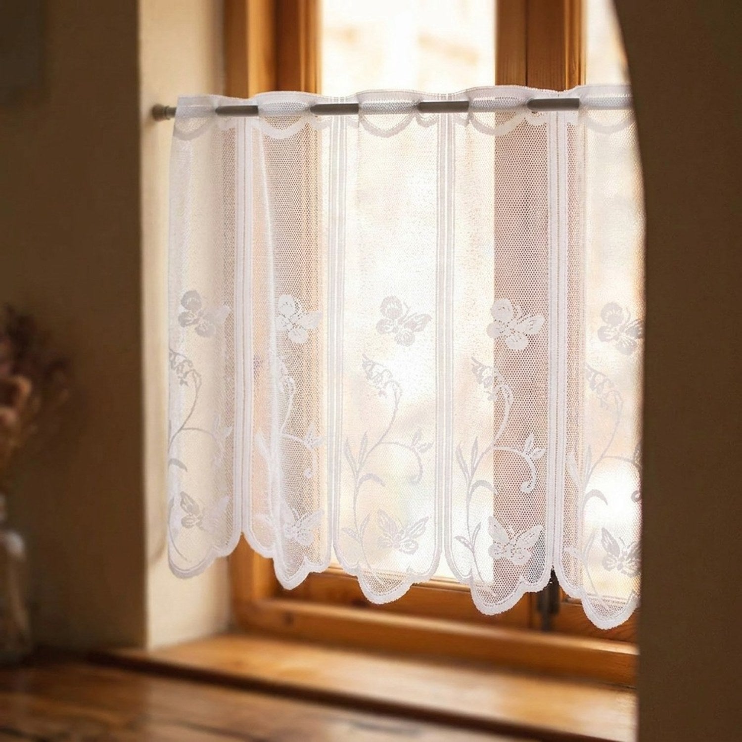 Voilage en dentelle blanche brodé de papillons suspendu à une fenêtre en bois lumineuse