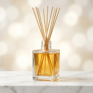 Diffuseur de parfum bâtonnets rotin flacon carré transparent sur étagère marbre fond blanc