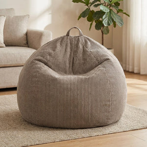 Housse de pouf poire en velours côtelé taupe posée dans un salon lumineux avec plaid et coussins
