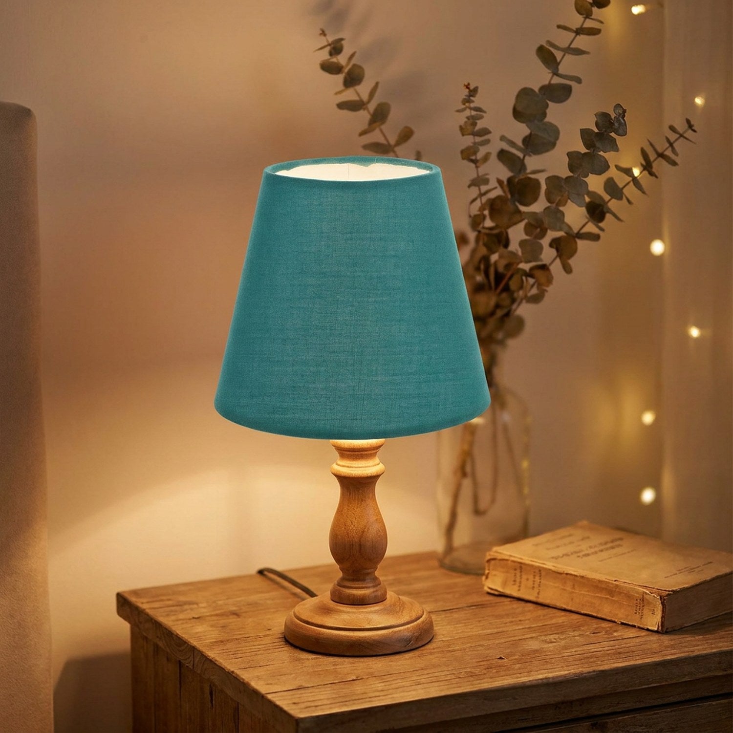 Abat-jour en tissu conique bleu canard sur une lampe de chevet en bois allumée
