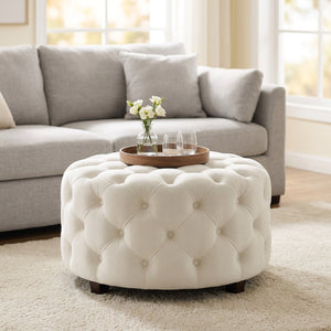 Tabouret pouf rond en velours blanc capitonné posé au sol dans un salon lumineux avec plateau et fleurs