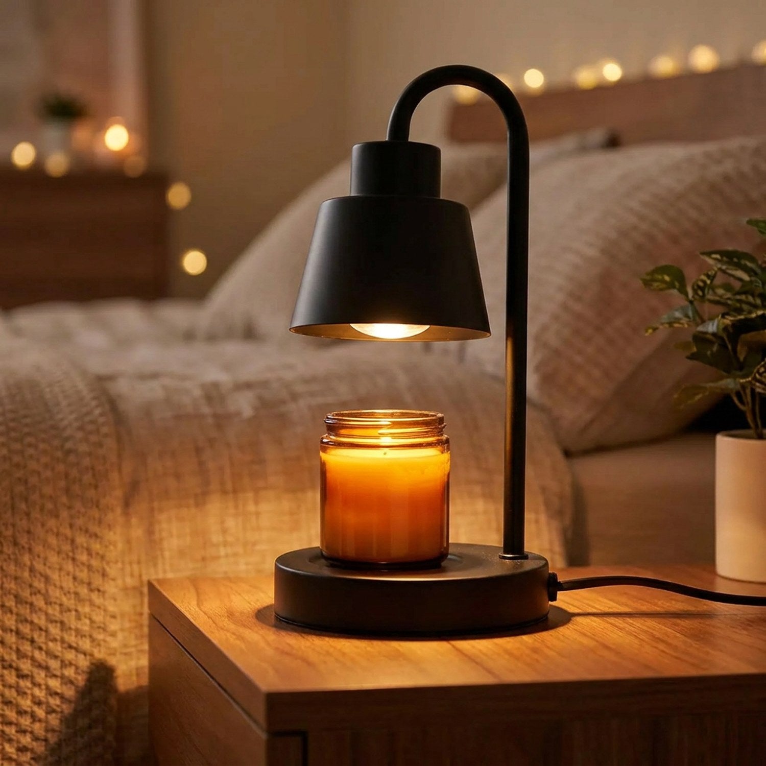 Lampe chauffe-bougie noire allumée posée sur une table de chevet en bois avec bougie parfumée