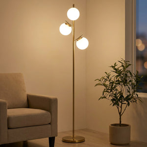 Lampadaire doré à 3 globes en verre dépoli allumé dans un salon chaleureux