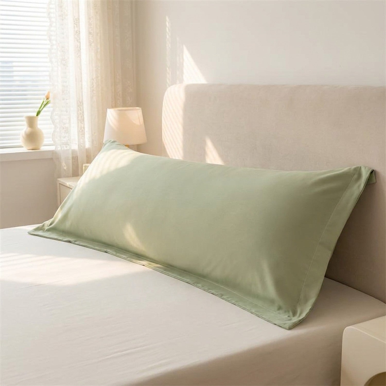 Taie de traversin longue en microfibre verte posée sur un lit dans une chambre douce et lumineuse
