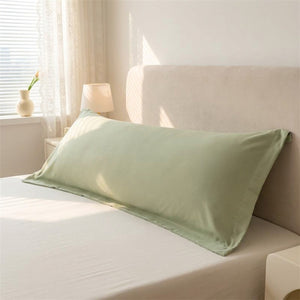 Taie de traversin longue en microfibre verte posée sur un lit dans une chambre douce et lumineuse