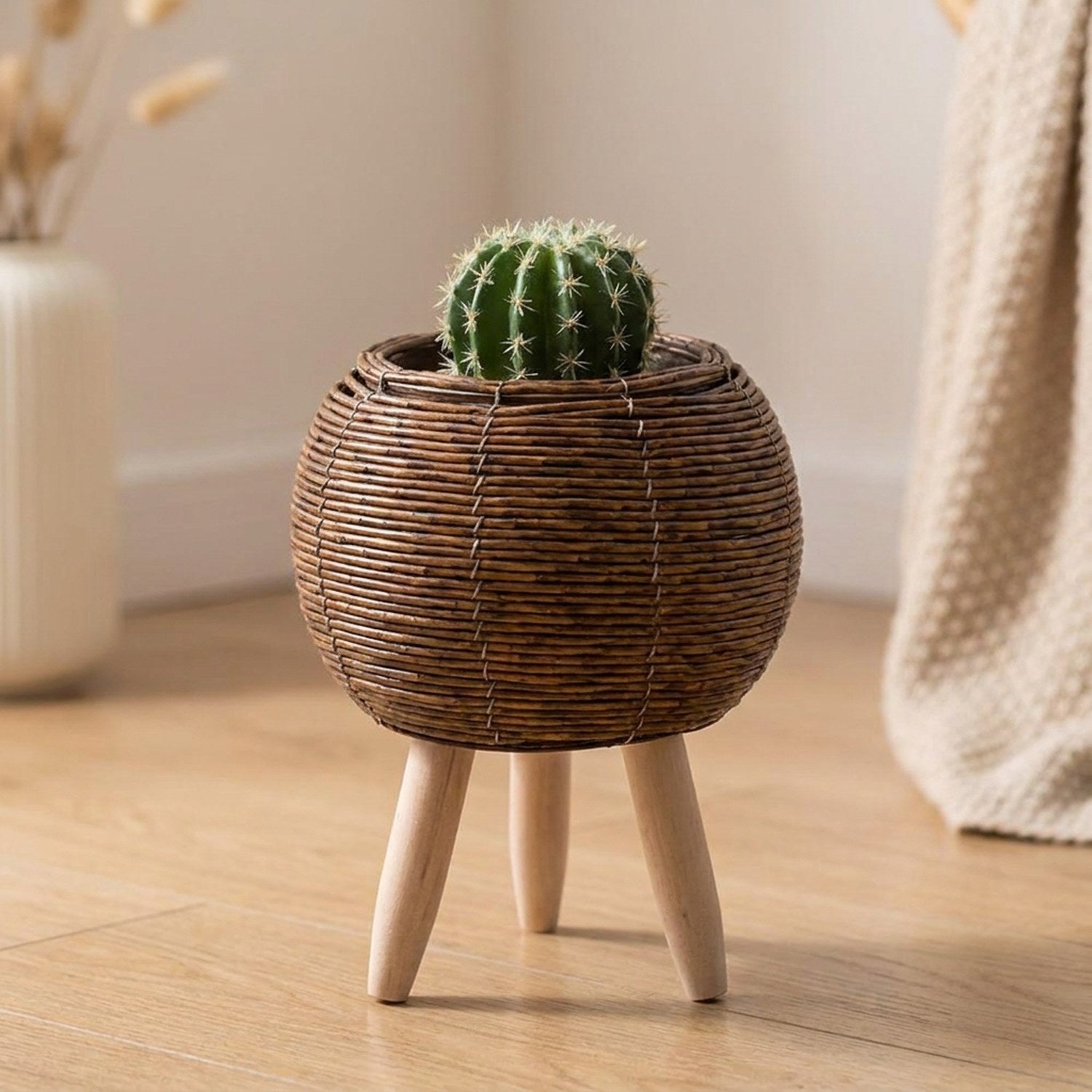 Cache-pot boule en rotin marron foncé sur pieds en bois avec petit cactus
