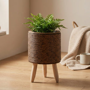 Cache-pot cylindrique en rotin marron foncé sur pieds en bois avec fougère