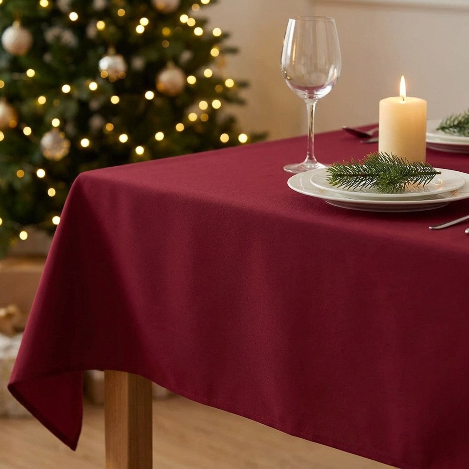 Gros plan sur le coin d'une table couverte de la nappe bordeaux avec assiette blanche, branche de sapin, verre à vin et bougie allumée