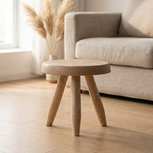 Tabouret rond en bois massif clair avec assise ronde et trois pieds tripode posé dans un salon lumineux