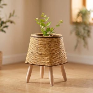 Cache-pot évasé en rotin naturel clair sur quatre pieds en bois avec plante