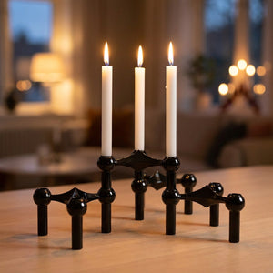 Chandelier modulaire en métal noir avec bougies fines allumées sur une table