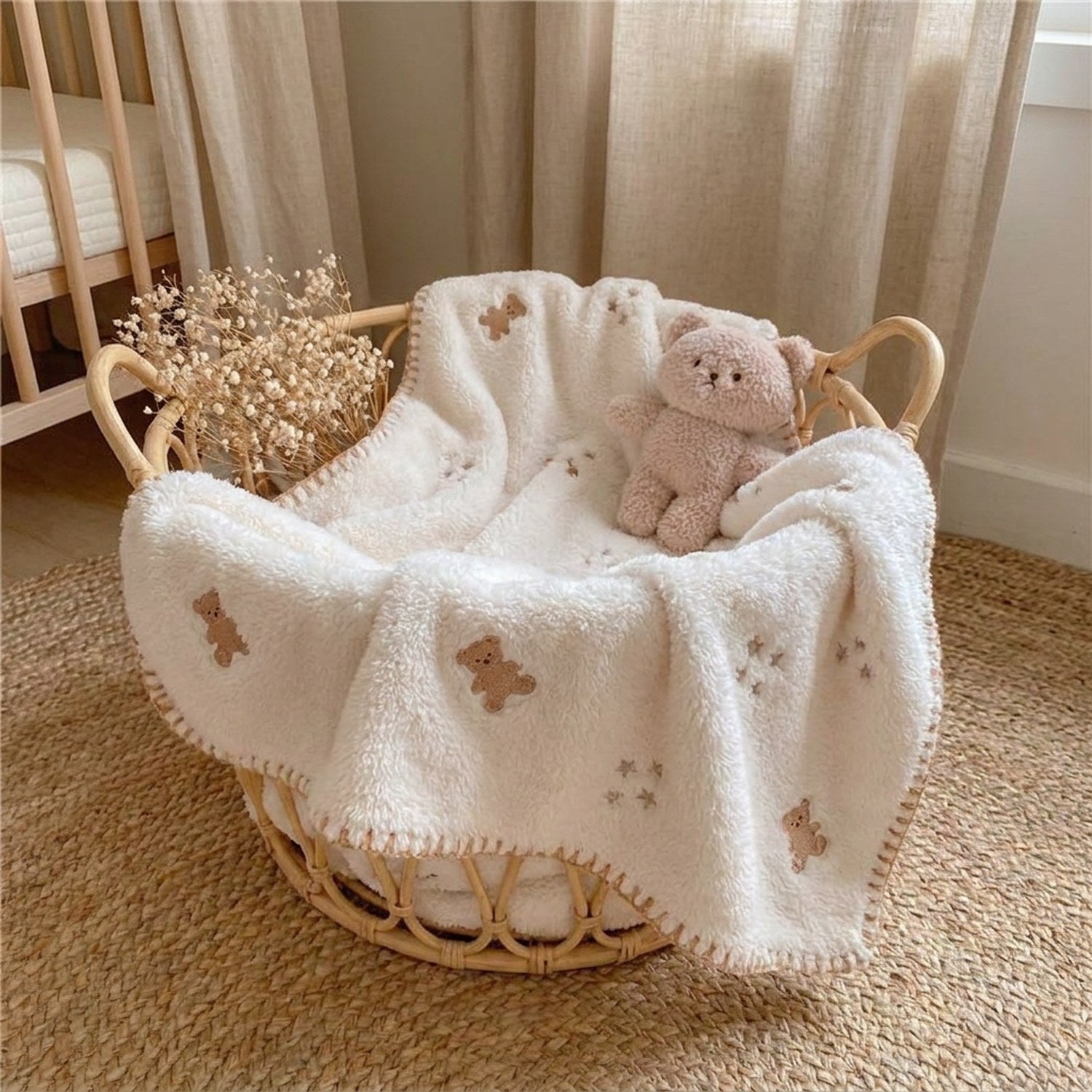 Couverture bébé en flanelle crème brodée de petits oursons posée dans un lit bébé douillet
