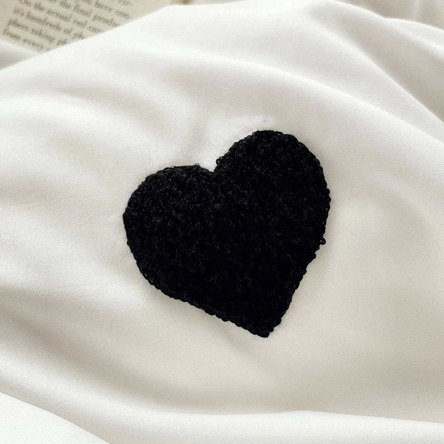 Gros plan sur le coeur brode noir sur le tissu blanc de la housse de couette