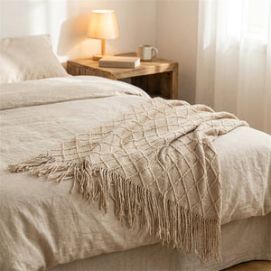 Plaid tricoté beige à franges drapé au pied d'un lit dans une chambre cocooning