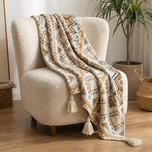 Plaid boho en maille beige et ocre à franges drapé sur un fauteuil bouclé dans un salon chaleureux