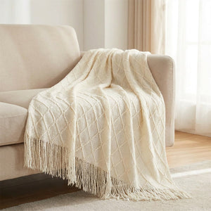 Plaid tricoté crème à franges drapé sur un canapé cocooning
