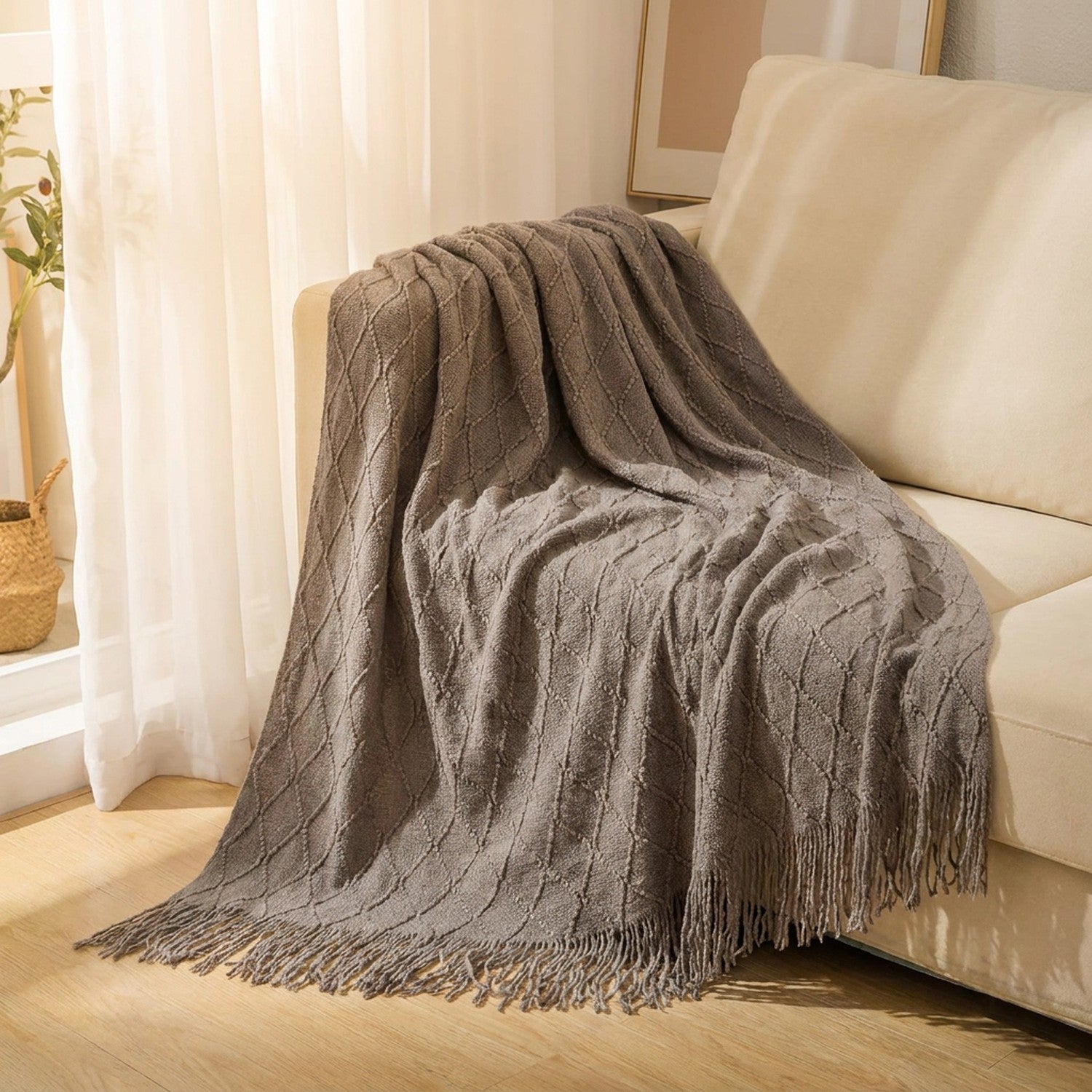 Plaid tricoté gris à franges drapé sur un canapé cocooning