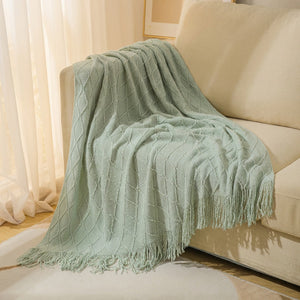 Plaid tricoté vert sauge à franges drapé sur un canapé cocooning
