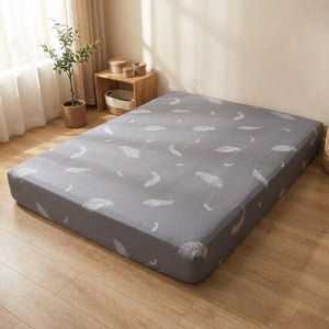 Housse de matelas intégrale à motif plumes grise posée sur un couchage dans une chambre lumineuse