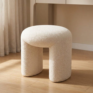 Pouf tabouret rond en tissu bouclé écru posé dans une chambre lumineuse près d'une coiffeuse