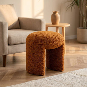 Pouf tabouret bouclé terracotta en repose-pieds près d'un fauteuil dans un salon
