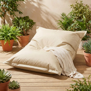 Pouf géant beige installé sur une terrasse ensoleillée avec plantes