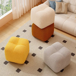 Les quatre couleurs du pouf bouclé blanc gris jaune et marron posées sur un tapis